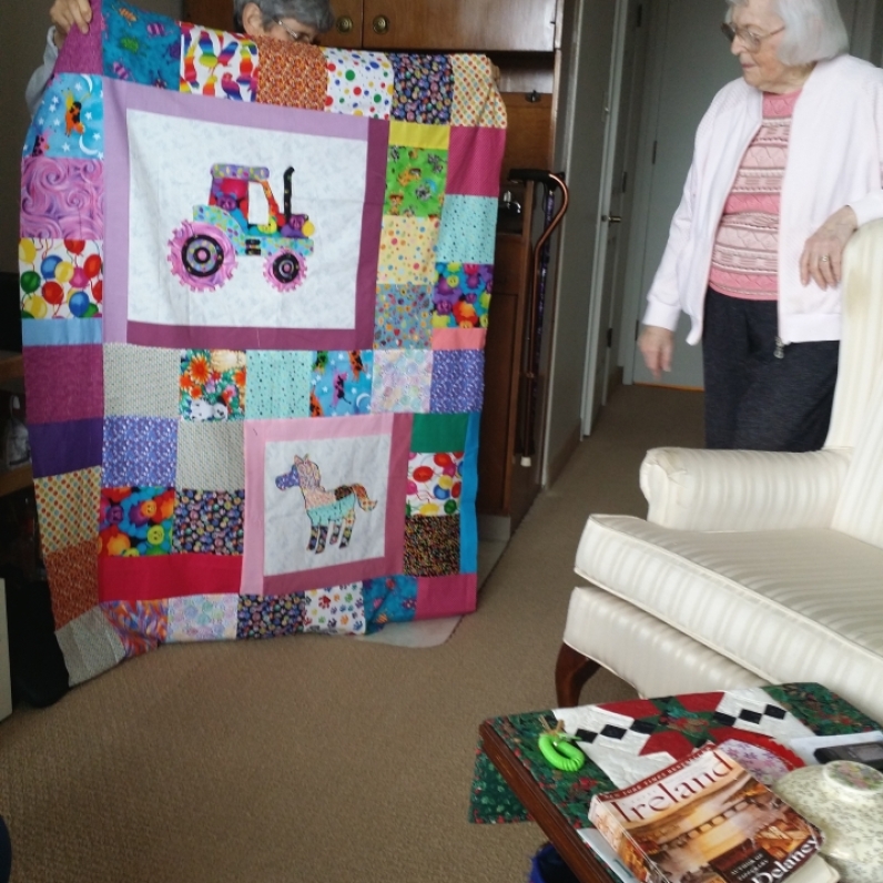 Laurie is hiding behind her quilt that she made for a friends child. Dolly admires it.